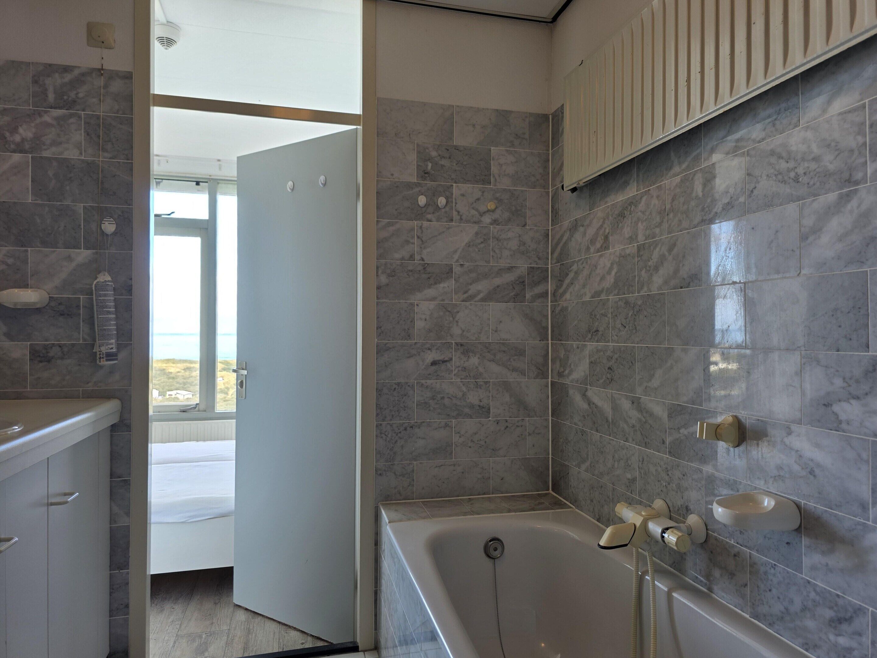 A modern bathroom with a bathtub, a shower, and a toilet. There is a window providing natural light and a view of the outdoors.