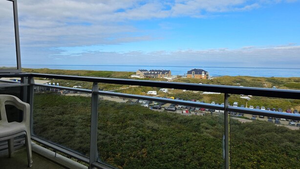 A balcony with a view of a beach, parked cars, and a building in the distance. - 2 Person Apartment With sea View (De Koog)