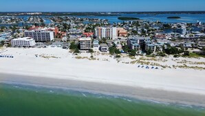 Vista aérea de un pueblo costero con propiedades frente a la playa, un puerto deportivo y una playa de arena.