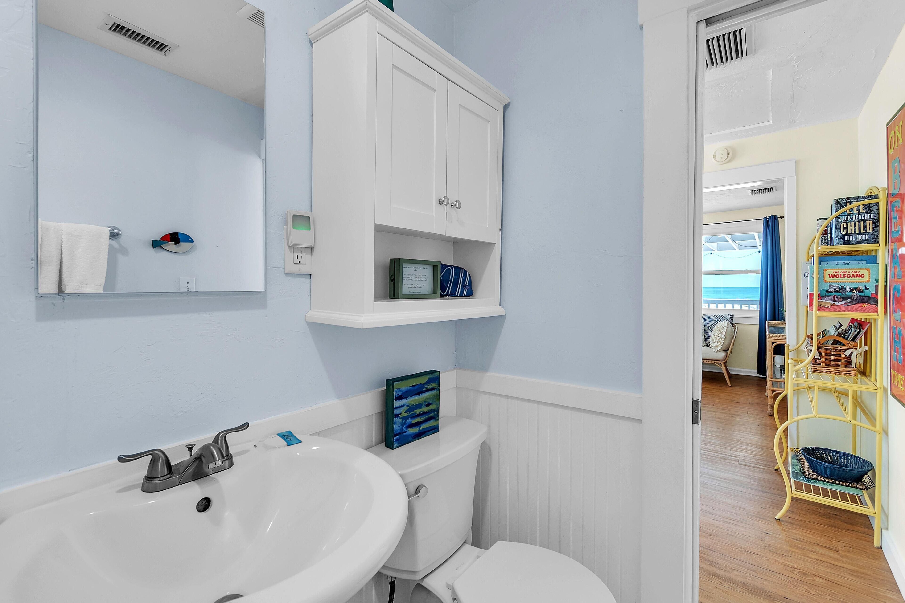 A bathroom with a white sink, toilet, and cabinet. There is a towel rack and a mirror on the wall.