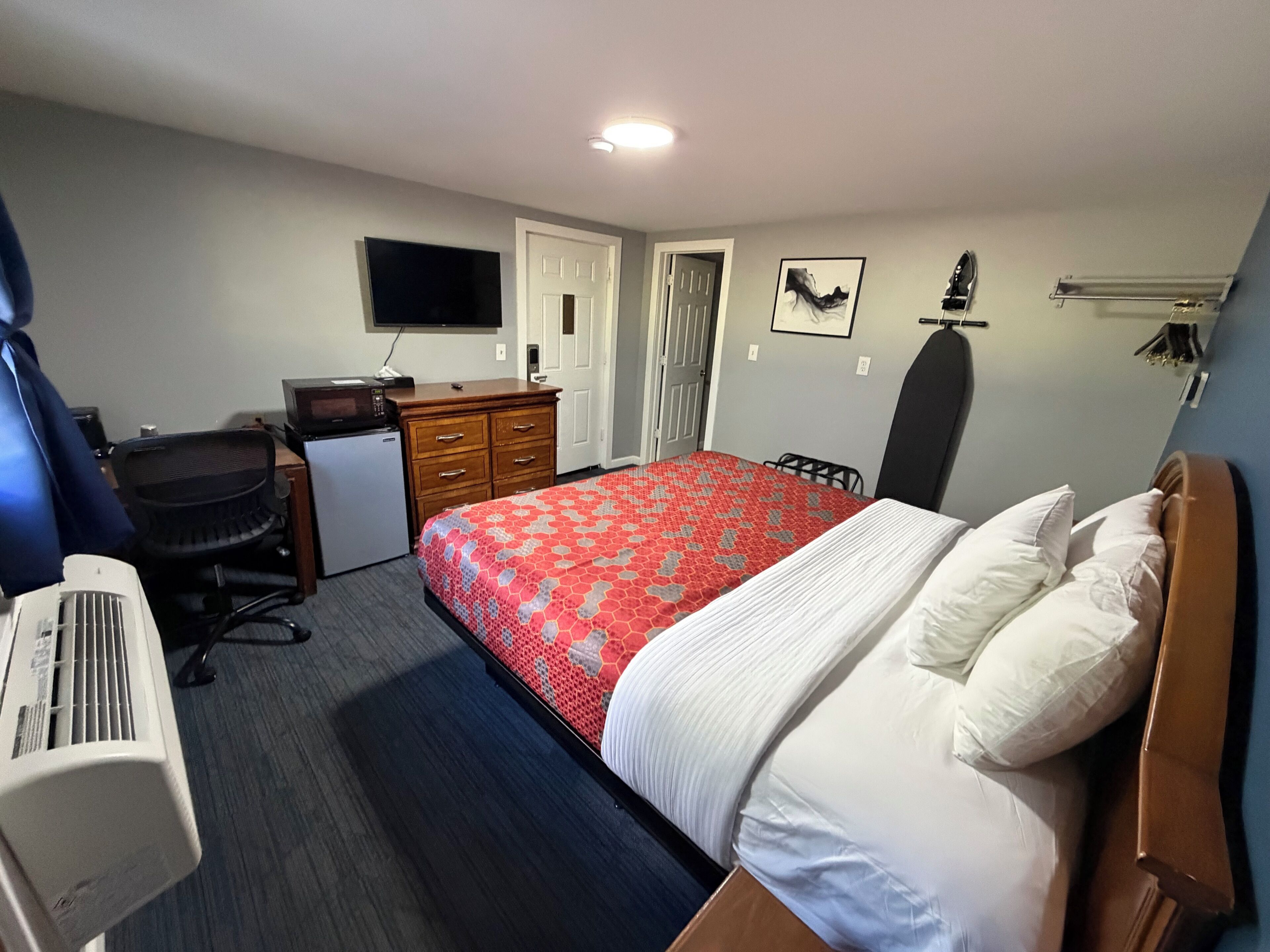 A hotel room with a bed, a desk, a chair, a TV, and a heater.