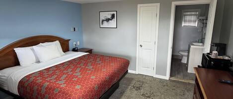 A bedroom with a bed, a nightstand, a dresser, a door leading to a bathroom, and a ceiling light.