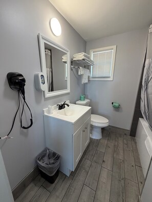 A bathroom with a white vanity, a toilet, a mirror, a hairdryer, and a trash bin.