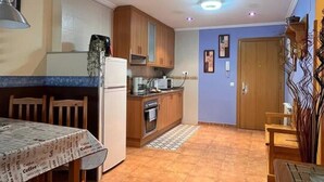 A compact kitchen with wooden cabinets, a refrigerator, a microwave, and a dining table with chairs. - 21A02 Charming Apartment with Garage by R2R (Aller)