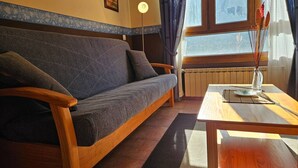 A room with a sofa, a wooden table, a floor lamp, and a window with curtains. - 21A02 Charming Apartment with Garage by R2R (Aller)