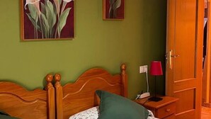 A room with a wooden bed, green walls, a nightstand with a lamp, and two paintings of flowers. - 21A02 Charming Apartment with Garage by R2R (Aller)
