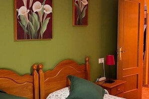 Una stanza con un letto di legno, pareti verdi, un comodino con una lampada e due dipinti di fiori.