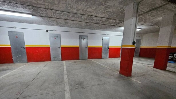 A parking garage with concrete floors, red and yellow painted walls, and numbered doors. - 21A02 Charming Apartment with Garage by R2R (Aller)