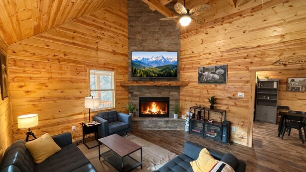 A cozy log cabin interior with a fireplace, a comfortable seating area, and a television mounted above the fireplace. - Family Sized Cabin Near RRG Hiking Trails + Hot Tub - Sleeps 9 (Stanton)