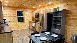 A wooden-paneled kitchen with a dining table set for four, stainless steel appliances, and a potted plant on the counter. - Family Sized Cabin Near RRG Hiking Trails + Hot Tub - Sleeps 9 (Stanton)