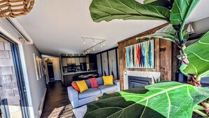 Ett modernt vardagsrum med en soffa, en stor grön växt och en färgstark, abstrakt tavla på väggen.
