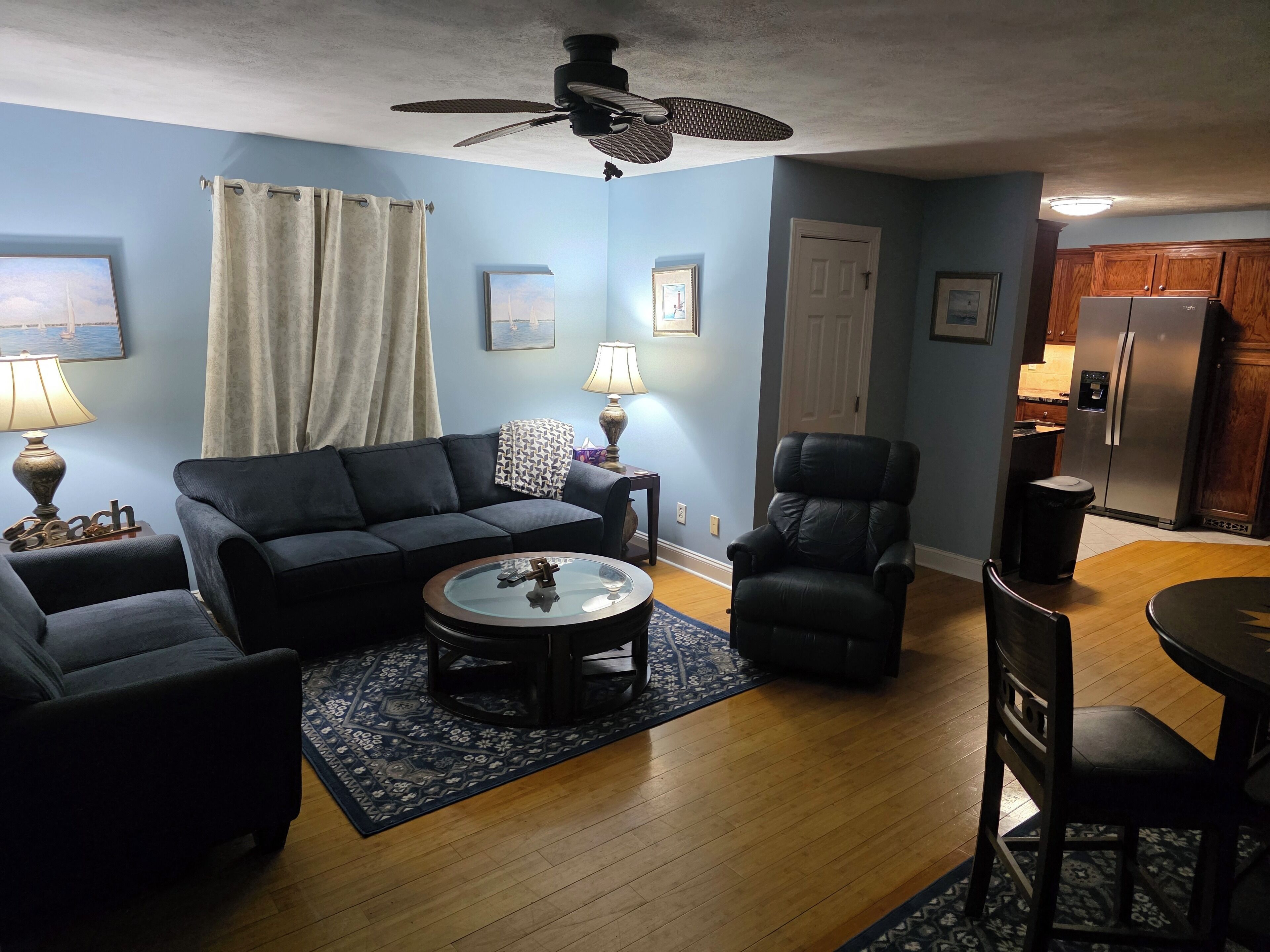 A living room with a sofa, armchairs, a coffee table, and a ceiling fan.