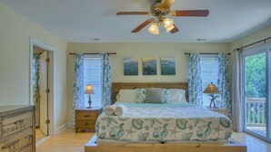 A bedroom with a wooden bed, a ceiling fan, and a view of the outdoors through large windows. - Pet Friendly! Ocean Views/2 king suites/ sleeps 12 (North Topsail Beach)