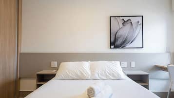 Habitación de hotel con cama, ropa de cama blanca, un cuadro colgado en la pared, mesitas de noche y un escritorio con silla.