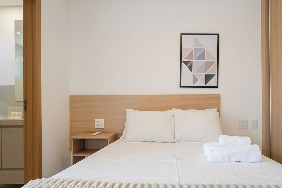 A hotel room with a bed, a nightstand, a framed picture on the wall, and a wooden headboard.