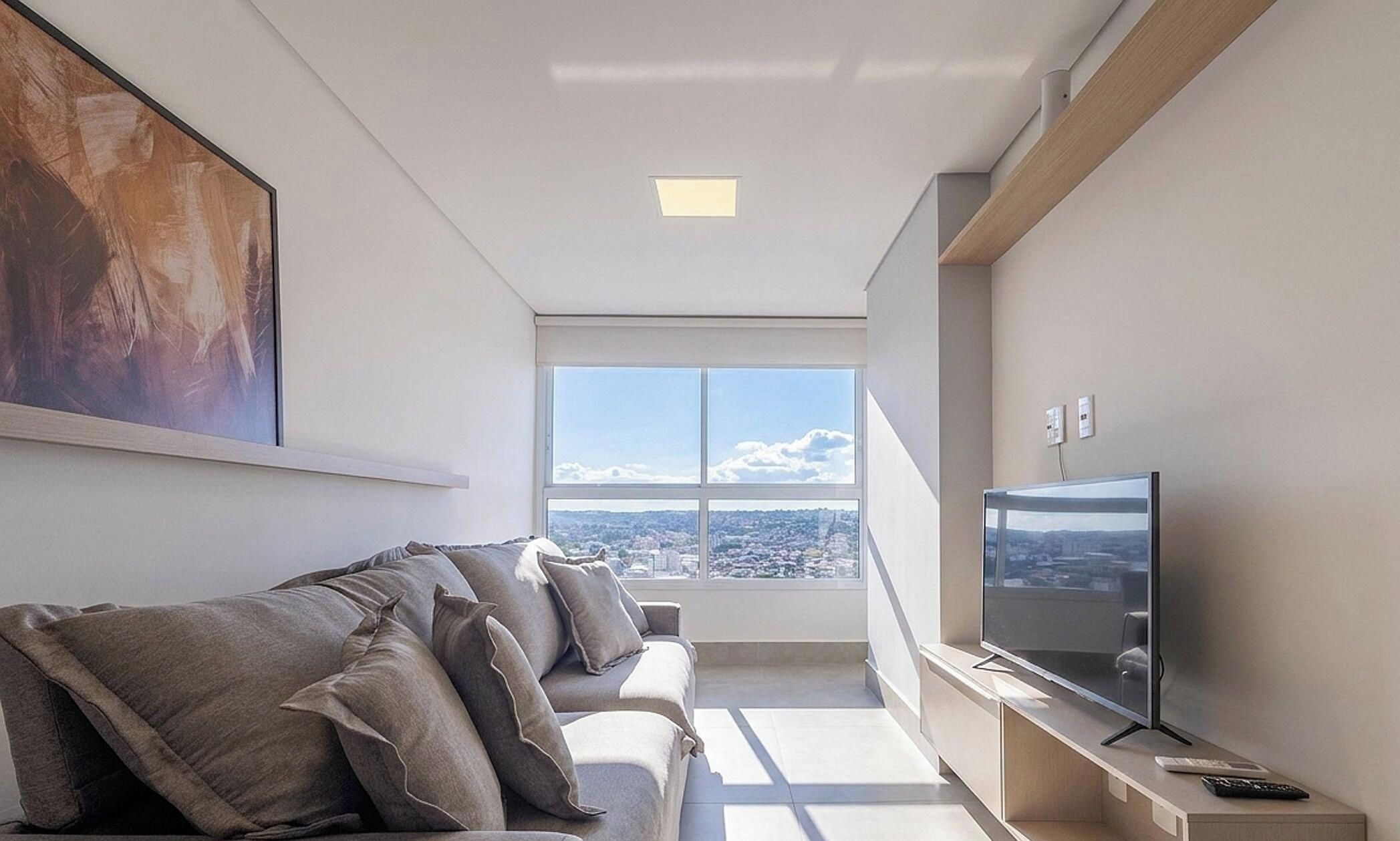 Sala de estar moderna com sofá, televisão de tela plana e uma grande janela com vista para a cidade.