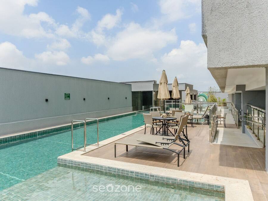 Un espace piscine aménagé sur le toit, avec des chaises longues et des parasols, entouré d’un bâtiment blanc.