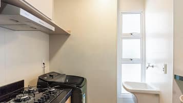 Cocina compacta con estufa a gas, horno integrado y ventana con vistas.