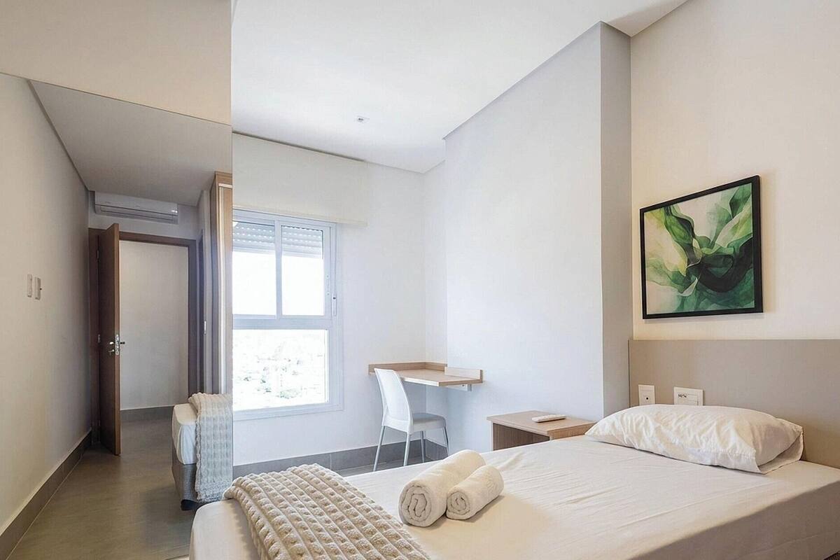 Una habitació d'hotel moderna amb un llit, un escriptori, una cadira i una finestra gran.
