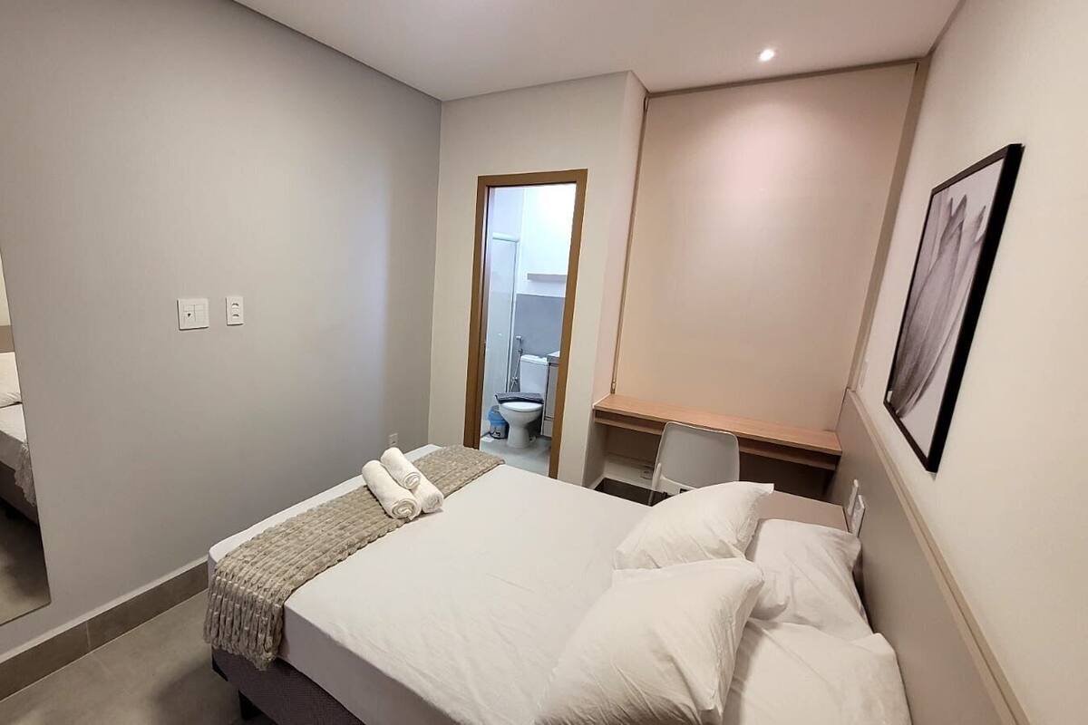A hotel room with a bed, bedside tables, a mirror, a door leading to a bathroom, and a framed picture on the wall.