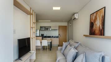 Una sala moderna con un televisor de pantalla plana, un sofá gris y una cocina al fondo.