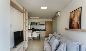 A modern living room with a flat-screen TV, a grey sofa, and a kitchen in the background. - Apts in a Building With Pool and Gym - GRL (Anapolis)