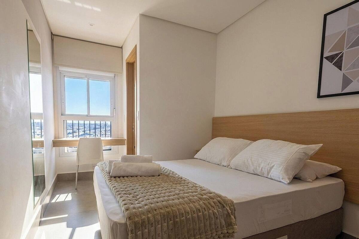 Un dormitori amb un llit, una finestra, una cadira i vista a la ciutat.