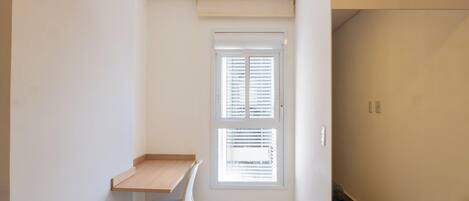 A room with a window, a small desk, and a chair.