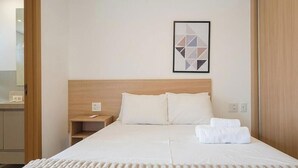 A hotel room with a bed, a nightstand, a framed picture on the wall, and a wooden headboard. - Apts in a Building With Pool and Gym - GRL (Anapolis)