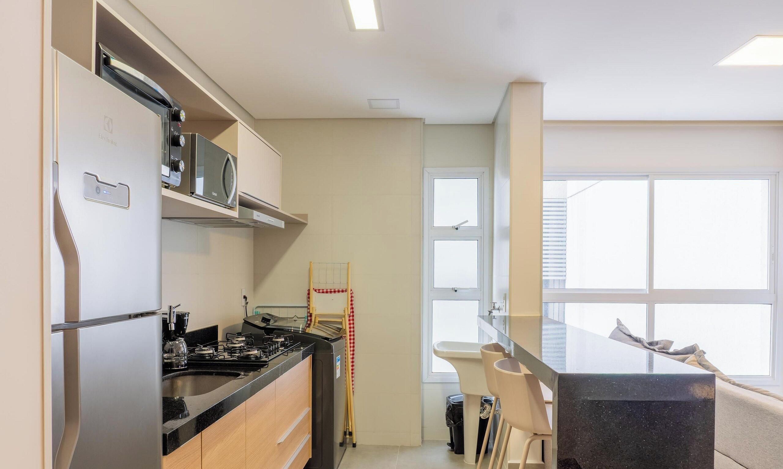 Eine moderne Küche mit Einbauherd, Mikrowelle und Backofen. Ein Fenster mit Jalousien, ein Spülbecken und eine kleine Kücheninsel mit Spiegel.