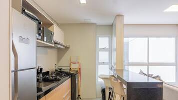 Eine moderne Küche mit Einbauherd, Mikrowelle und Backofen. Ein Fenster mit Jalousien, ein Spülbecken und eine kleine Kücheninsel mit Spiegel.