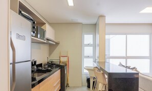 Une cuisine moderne équipée d’une cuisinière, d’un four à micro-ondes et d’un four encastrés. On y trouve une fenêtre avec des stores, un évier et un petit îlot central avec un miroir.