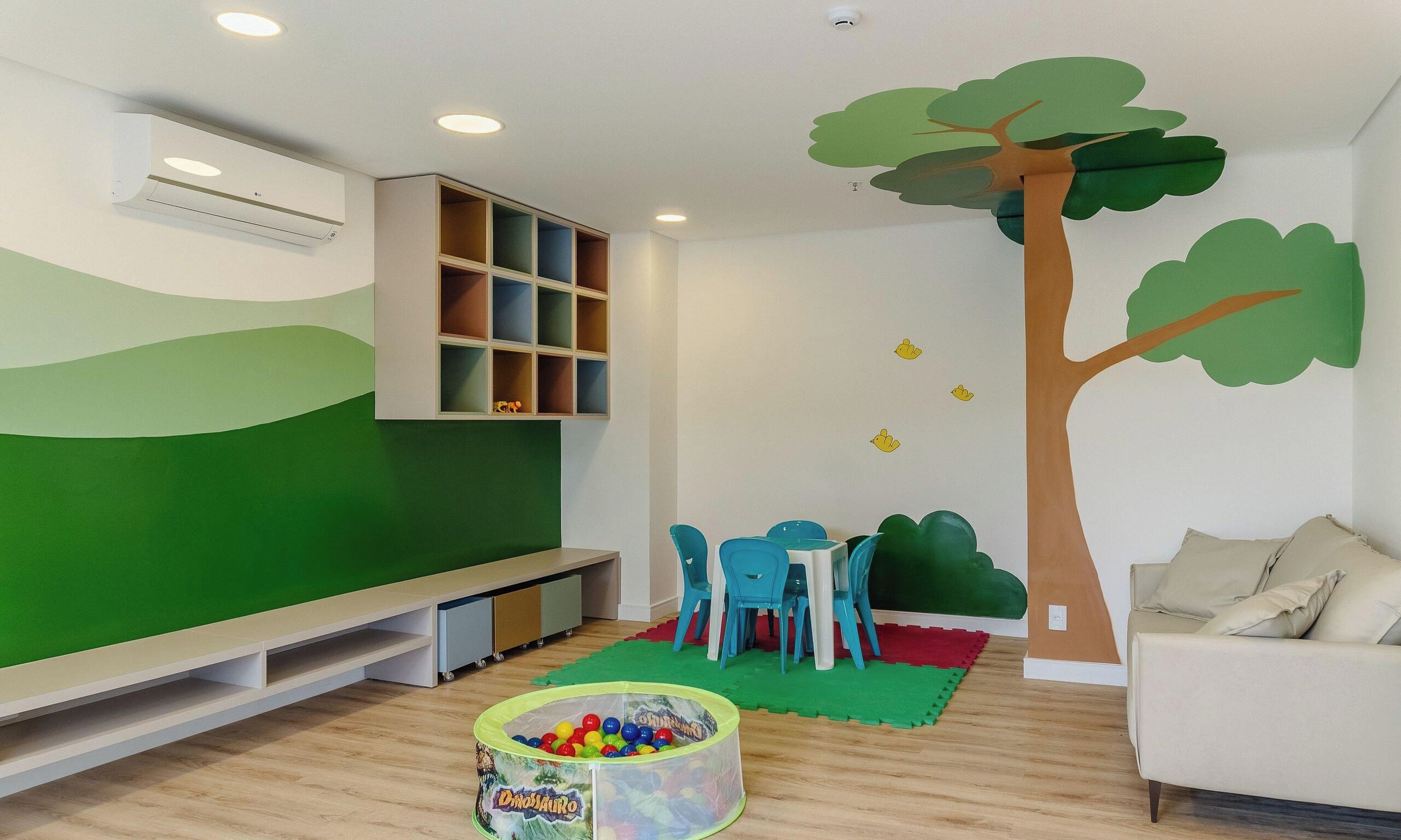 A children's play area with a green wall, a tree mural, a bench, a table with chairs, and a ball pit.