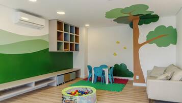A children's play area with a green wall, a tree mural, a bench, a table with chairs, and a ball pit.