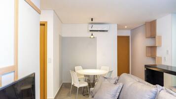 A modern living room with a sofa, a dining table with chairs, a TV, and a kitchen area with cabinets.