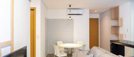 Una sala de estar moderna con un sofá, una mesa de comedor con sillas, un televisor y una zona de cocina con armarios.