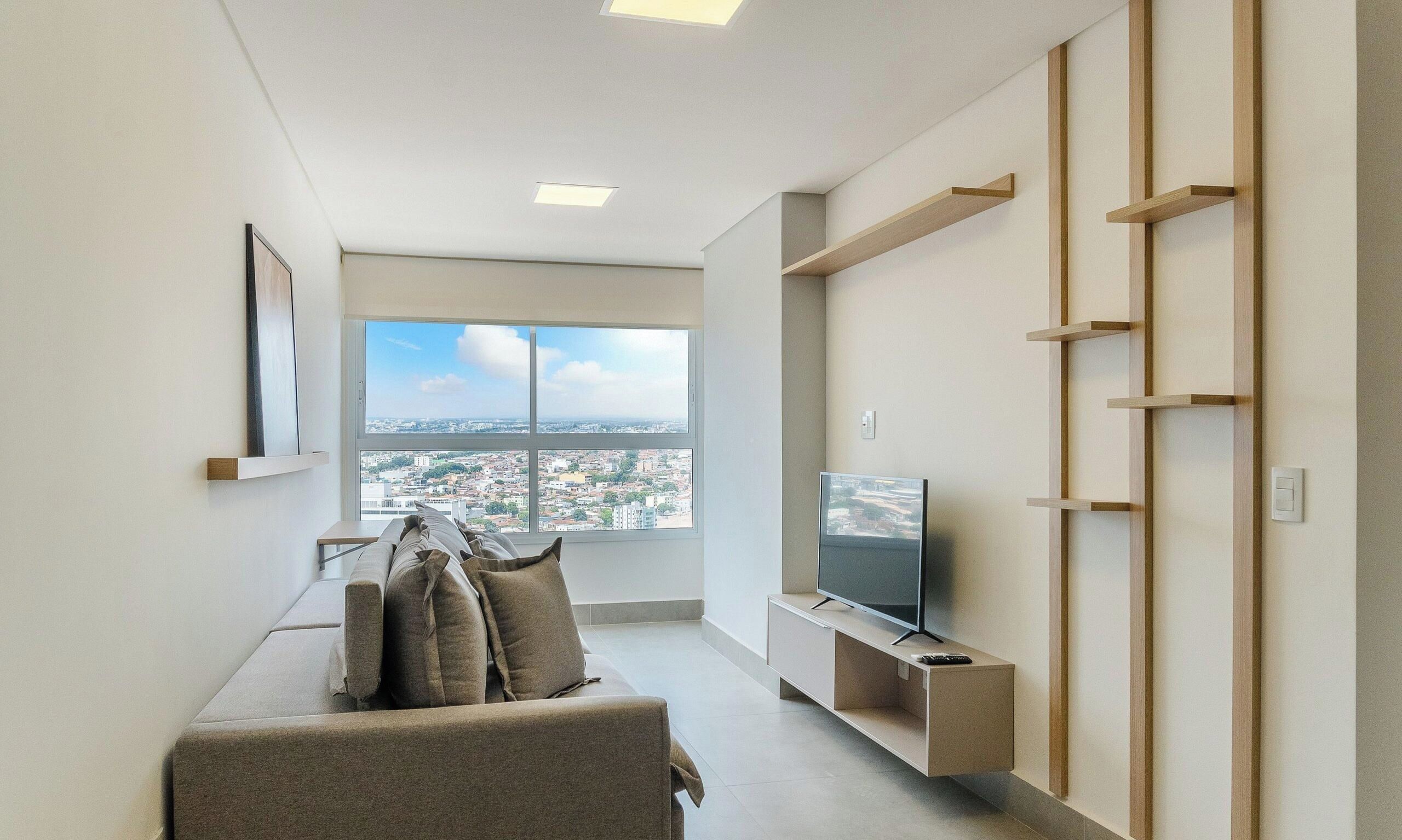 Sala de estar moderna com sofá, televisão e vista para a cidade.