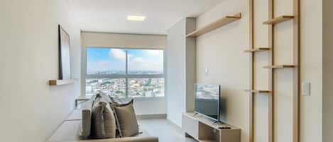 Sala de estar moderna com sofá, televisão e vista para a cidade.