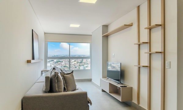 Ein modernes Wohnzimmer mit einer Couch, einem Fernseher und Blick auf die Stadt.