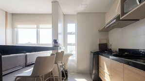 A modern kitchen with a black countertop, white cabinets, and a built-in stove. There are bar stools and a window providing natural light. - Apts in a Building With Pool and Gym - GRL (Anapolis)
