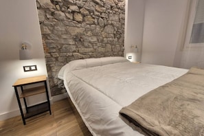 Une chambre avec un mur en pierre, un lit avec une literie blanche, une table de chevet en bois et des lampes de chevet.