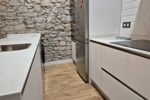 Una cocina con pared de piedra, electrodomésticos de acero inoxidable y muebles de cocina blancos.