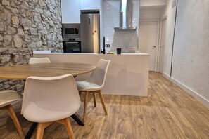 Una cocina moderna con un muro de acento de piedra, una mesa de comedor de madera y sillas blancas.