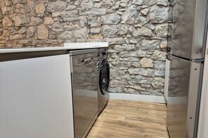 Una cocina compacta con pared de piedra, lavadora y refrigerador.