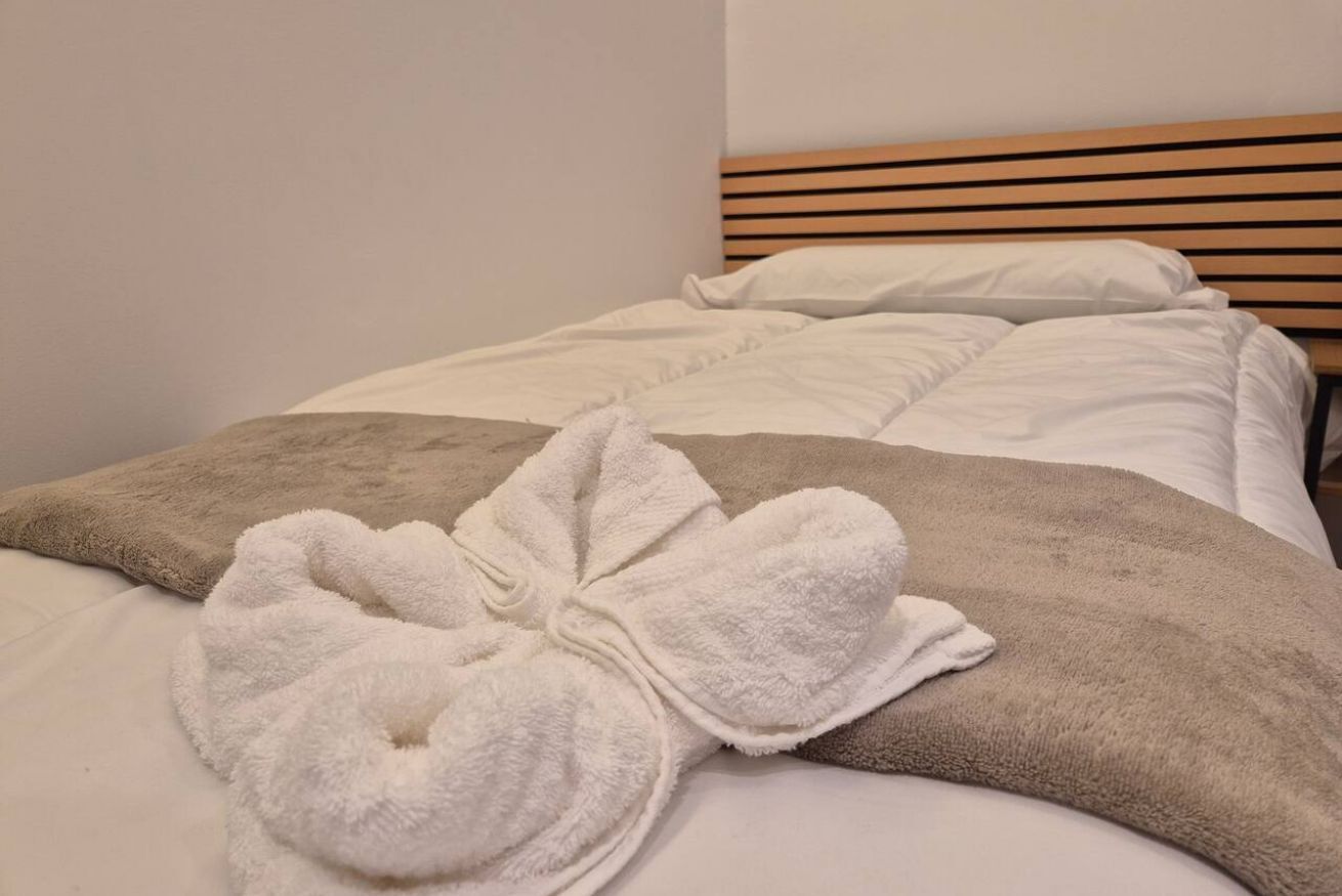 Una cama con una manta blanca y marrón, una toalla blanca y un cabecero de madera.