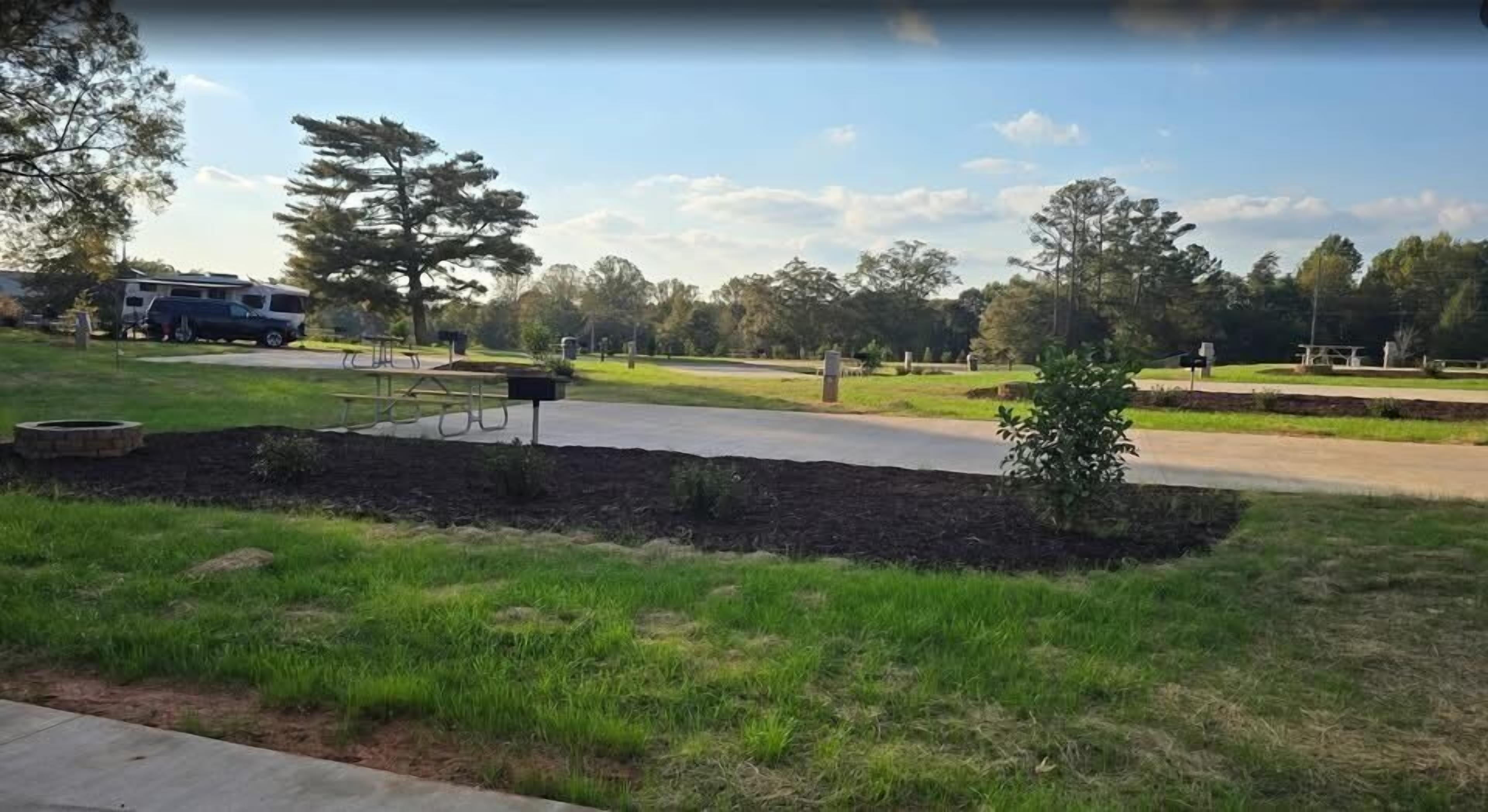 A park with picnic tables, a small tree, and a paved path.