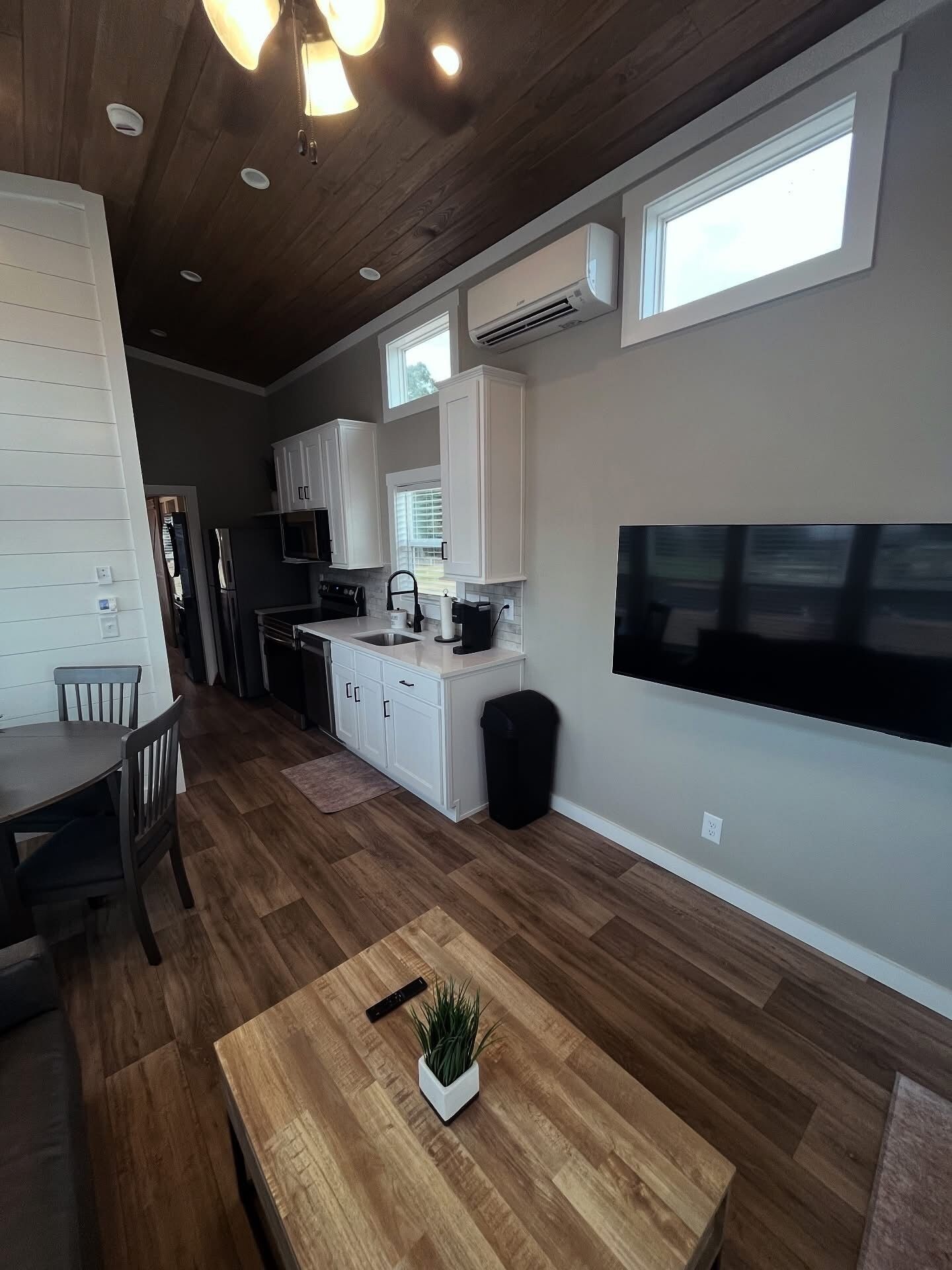 A modern kitchen with white cabinets, a large window, and a flat-screen TV mounted on the wall.