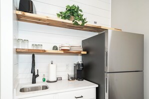 A kitchen with a stainless steel refrigerator, a coffee maker, a sink, and wooden shelves with glass jars and plates. - Carolina Camp Cedar (Pickens)