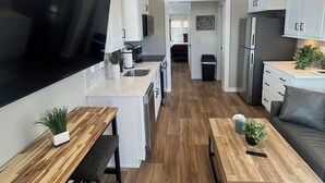 A modern kitchen with white cabinets, a large TV, wooden flooring, and a dining area with a bench and coffee table. - Carolina Camp Cedar (Pickens)