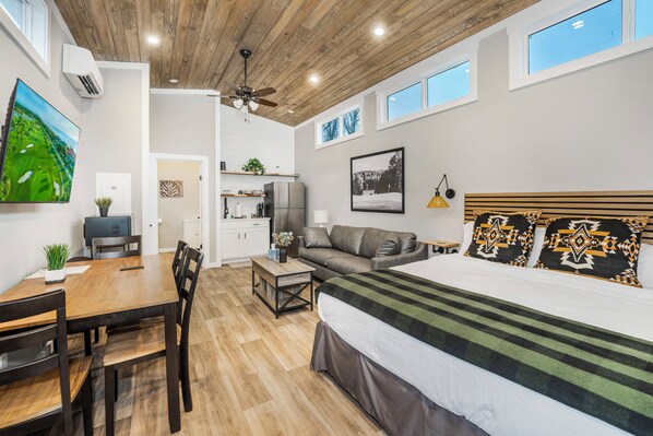 A modern bedroom with a large bed, a ceiling fan, and a view of the outdoors through a window. - Carolina Camp Cedar (Pickens)